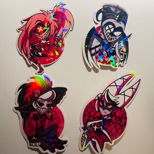 May include: Four holographic stickers featuring characters from the animated series "Hazbin Hotel". The stickers are on a white background. The characters are: Angel Dust, a red-haired demon with a cross on his forehead; Alastor, a tall, slender demon with a deer skull for a head;  Vaggie, a demon with a red and black dress and a black and white mask; and Charlie, a demon with a red and black dress and a black and white mask.