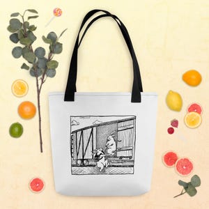 Può includere: Borsa tote bianca con manici neri. Presenta un'illustrazione in bianco e nero di due conigli vicino a un vagone ferroviario. Uno sale, l'altro è a terra. La borsa è circondata da frutta.