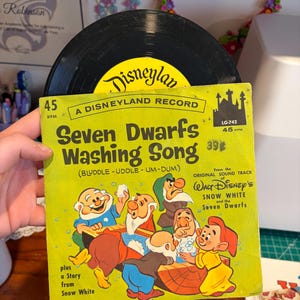 May include: Vintage Disneyland record featuring the "Seven Dwarfs Washing Song" from Snow White. The album cover is lime green with illustrations of the seven dwarfs. The record label is yellow with the Disneyland logo.