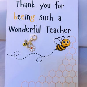 May include: A white greeting card with the message "Thank you for beeing such a Wonderful Teacher." A bee and flower charm is attached. A cartoon bee flies near a honeycomb design.