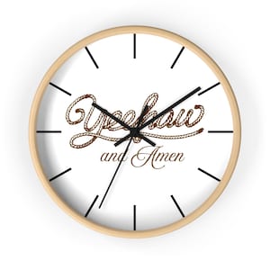 May include: A round wall clock with a light wood frame and a white face. The clock features black hour markers and black hands. The center of the clock displays the text Yeehaw and Amen, with the word Yeehaw styled to look like a brown rope.