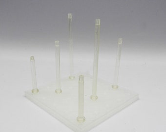 May include: A clear plastic stand with six clear plastic rods. The stand has a square base and the rods are evenly spaced around the base.