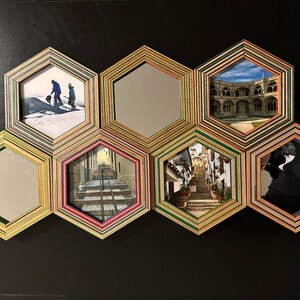 Pu&ograve; includere: Un decoro da parete realizzato con cornici esagonali con diverse immagini e specchi. Le cornici sono realizzate in legno stratificato con una variet&agrave; di colori, tra cui verde, marrone e rosa. Le immagini includono un paesaggio innevato, una strada cittadina, un edificio con archi e uno specchio.