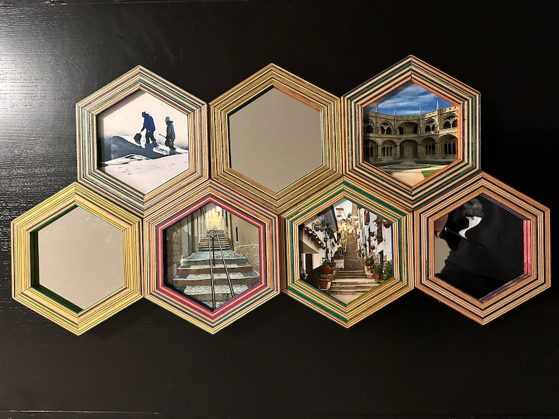 Pu&ograve; includere: Un decoro da parete realizzato con cornici esagonali con diverse immagini e specchi. Le cornici sono realizzate in legno stratificato con una variet&agrave; di colori, tra cui verde, marrone e rosa. Le immagini includono un paesaggio innevato, una strada cittadina, un edificio con archi e uno specchio.