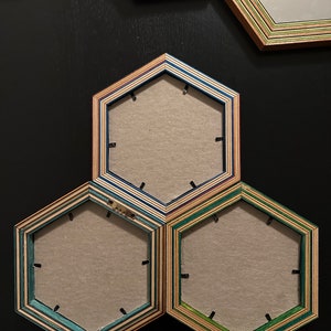 Pu&ograve; includere: Tre cornici per foto esagonali in legno con diversi strati di colore. Le cornici sono disposte a forma di piramide, con la cornice superiore che &egrave; la pi&ugrave; grande e le due cornici inferiori che sono pi&ugrave; piccole. Le cornici sono vuote e hanno uno sfondo marrone chiaro.
