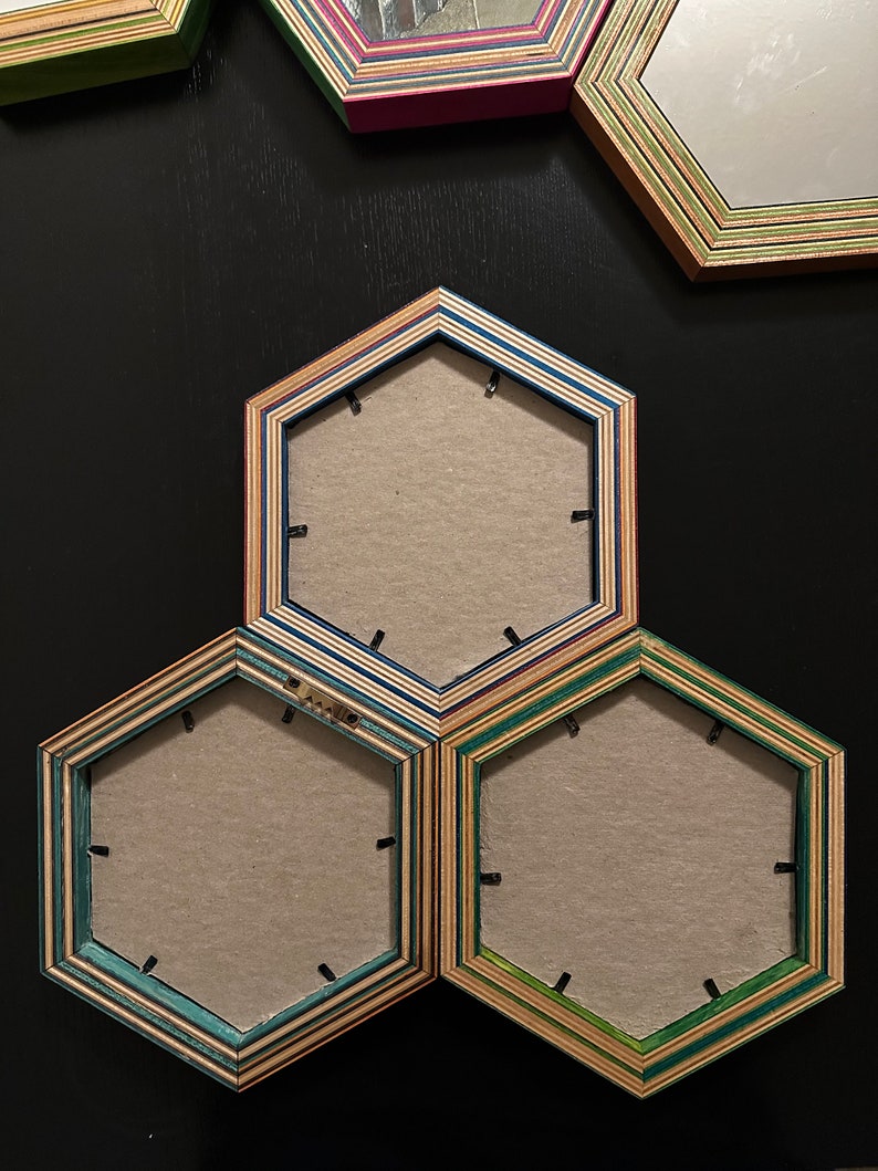 Pu&ograve; includere: Tre cornici per foto esagonali in legno con diversi strati di colore. Le cornici sono disposte a forma di piramide, con la cornice superiore che &egrave; la pi&ugrave; grande e le due cornici inferiori che sono pi&ugrave; piccole. Le cornici sono vuote e hanno uno sfondo marrone chiaro.