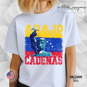 May include: White t-shirt with a graphic design featuring a person holding a hammer and the text "ABAJO CADENAS" in red, yellow, and blue. The graphic also includes a stylized image of the Venezuelan flag.