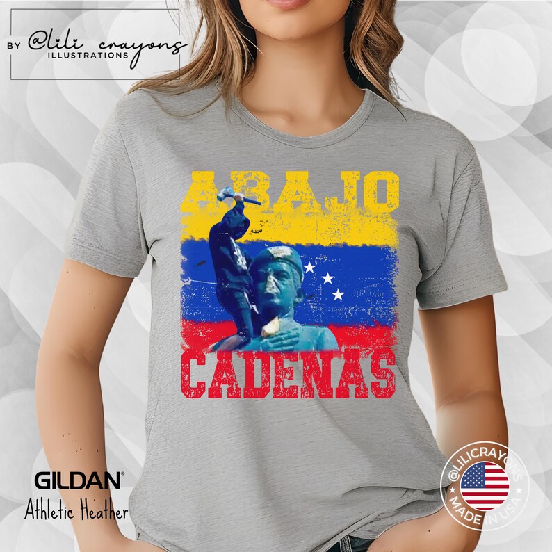 May include: A gray t-shirt with a graphic design featuring a person breaking chains with a hammer. The graphic includes the text "ABAJO CADENAS" and the colors of the Venezuelan flag.