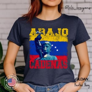 May include: A navy blue t-shirt with a distressed yellow and red graphic of a statue and the text "ABAJO CADENAS". The graphic also includes the Venezuelan flag.