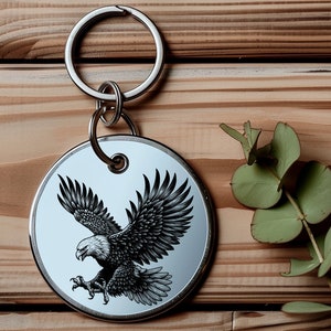 May include: A silver key chain with a round metal tag featuring a black and white illustration of an eagle in flight.