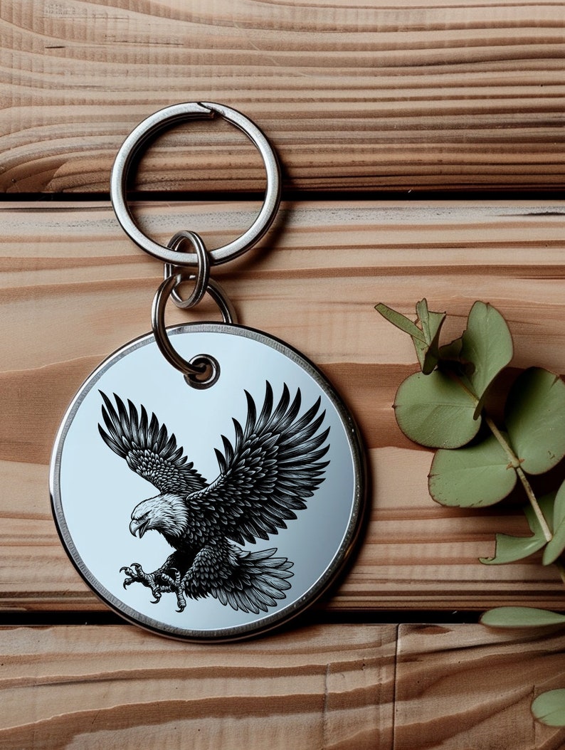 May include: A silver key chain with a round metal tag featuring a black and white illustration of an eagle in flight.