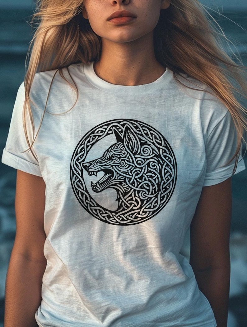 May include: White t-shirt with a black and white graphic of a wolf's head inside a Celtic knot design.