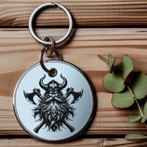May include: A silver keychain with a round metal charm featuring a black and white illustration of a Viking warrior with a horned helmet and crossed axes.