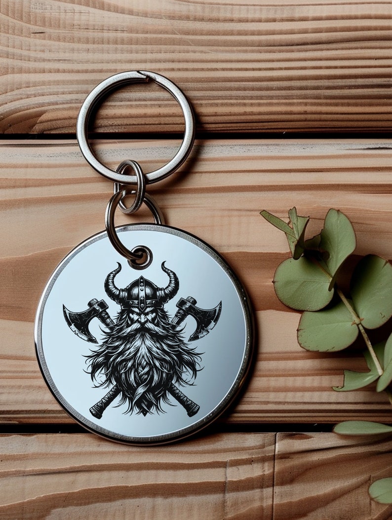 May include: A silver keychain with a round metal charm featuring a black and white illustration of a Viking warrior with a horned helmet and crossed axes.