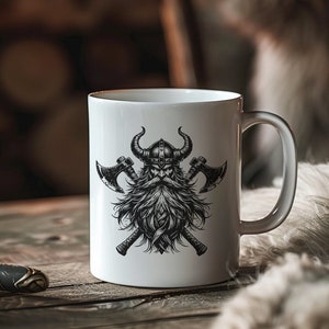 May include: White ceramic mug with a black and white illustration of a Viking warrior with crossed axes. The warrior has a beard and is wearing a horned helmet.