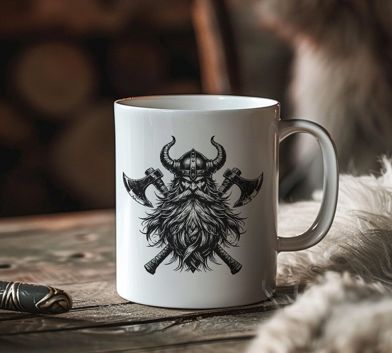 May include: White ceramic mug with a black and white illustration of a Viking warrior with crossed axes. The warrior has a beard and is wearing a horned helmet.