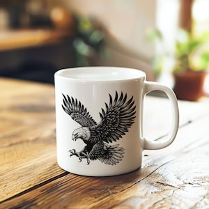 May include: White ceramic mug with a black and white illustration of an eagle in flight. The eagle is depicted with its wings spread wide and its talons extended.