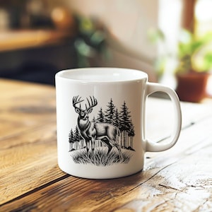 Może przedstawiać: Biały kubek ceramiczny z czarno-białym rysunkiem jelenia stojącego w lesie. Jeleń ma duże poroże i patrzy w lewo. Las składa się z sosen.