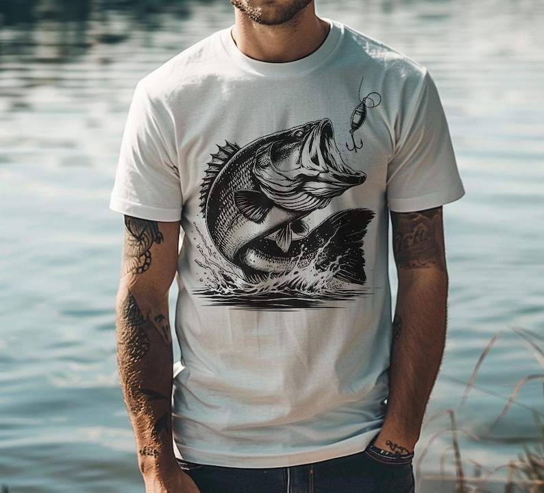 K&ouml;nnte beinhalten: Wei&szlig;es T-Shirt mit einem schwarz-wei&szlig;en Motiv eines Gro&szlig;maulbarsches, der mit einem Angelk&ouml;der im Maul aus dem Wasser springt.