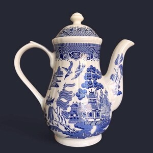 May include: A white and blue ceramic teapot with a lid. The teapot features a classic Willow pattern with a landscape scene, including pagodas, trees, and birds. The handle and spout are curved. The teapot is a classic piece of tableware.