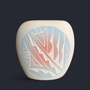 Könnte beinhalten: Eine cremefarbene Keramikvase mit abgerundeter Form. Die Vase hat ein kreisförmiges Design mit hellblauem Hintergrund und einer stilisierten Illustration in Weiß und Orange. Das Design scheint Segel oder abstrakte Formen darzustellen.