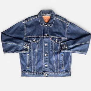 May include: A classic blue denim jacket with a button-up front, two chest pockets, and two side pockets. The jacket features a collar and is made of durable denim material. A small red tag is visible on the chest pocket.