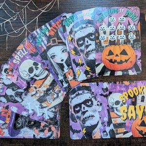 May include: A selection of Halloween-themed cards featuring illustrations of a skull, a witch, and a monster. The cards are purple, orange, and white, with text reading "A7 Spooky Challenges" and "Spooky Mini Savers".