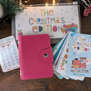 May include: A pink leather wallet with a snap closure, a set of Christmas-themed cards with a train and the text "The Christmas Edition", and a card with the text "The 24 Challenge Christmas Edition" with numbers 1-24.