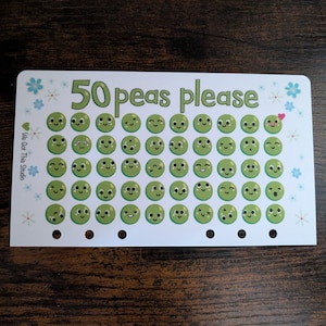 May include: A white card with 50 green pea stickers with different facial expressions. The card says "50 peas please" and has a small heart on one of the peas. The card has a white background with blue flowers and the text "We Got This Studio".