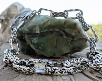 May include: A silver chain bracelet with a detailed, textured design. The links are large and oval-shaped, with a leaf-like pattern.