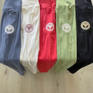 May include: Five pairs of yoga pants in different colors: blue, white, red, green, and black. Each pair has a pocket on the side with an embroidered elephant logo.