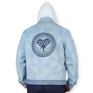 Pu&ograve; includere: Una giacca di jeans blu chiaro con una felpa con cappuccio bianca sotto. La giacca ha un design di elefante blu e bianco sul retro con il testo "TEIFF The Elephant in the Room". La giacca ha anche un design a chiave greca blu e bianco intorno all'orlo inferiore.