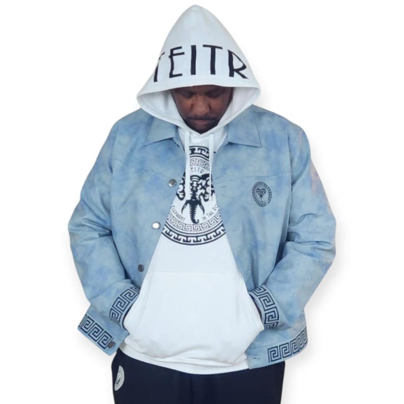 Pu&ograve; includere: Una giacca di jeans blu chiaro con una felpa bianca sotto. La giacca ha un motivo tie-dye e disegni a chiave greca sui polsini e sul collo. La felpa ha una grafica in bianco e nero di una creatura mitologica con il testo "EITR" sul cappuccio.