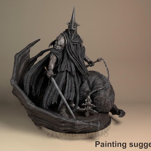 Op de afbeelding: Een gedetailleerd, donkergrijs beeld van een figuur in harnas, met een zwaard en ketting, bovenop een beest. De figuur draagt een hoge, puntige helm en een vloeiende cape. De basis is getextureerd, met "Painting suggestion" onderaan.