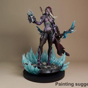 Op de afbeelding: Gedetailleerd beeldje van een fantasiekarakter, met een vrouwelijk figuur in een paarse en zwarte outfit, met een boog en een klauwachtige handschoen. Het figuur staat op een basis met blauwe kristalformaties. Het ontwerp suggereert een krijger- of boogschutterthema.