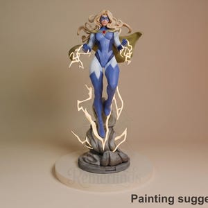 Peut inclure: Figurine d'une super-héroïne en costume bleu et blanc avec une cape dorée. La figurine est posée, les bras tendus, émettant des éclairs. La base est une structure en forme de pierre sur une plateforme circulaire blanche. Le texte "Suggestion de peinture" est en bas.