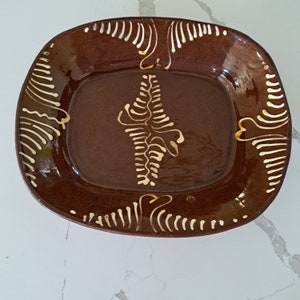 Puede incluir: Un plato de servir de cerámica marrón con un glaseado blanco. El plato tiene un diseño decorativo de hojas y espirales estilizadas.