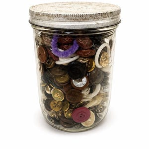 May include: A clear glass mason jar filled with a variety of assorted buttons in different colors, shapes, and sizes, including brown, black, gold, white, and a single maroon button, topped with a weathered, textured silver metal lid.