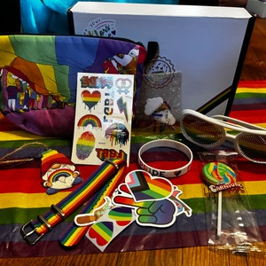 May include: A rainbow-themed gift box with a variety of items, including a rainbow-patterned pouch, a rainbow-colored wristband, a rainbow-colored lollipop, a pair of rainbow-colored sunglasses, and a set of rainbow-themed temporary tattoos.