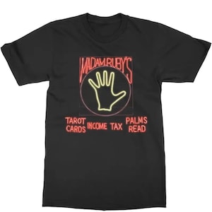 May include: Black t-shirt with a neon-style graphic. The graphic features the text "MADAM RUBY'S" above a hand outline within a circle. Below, it reads "TAROT CARDS INCOME TAX PALMS READ".