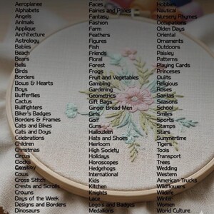 May include: An embroidered hoop art piece with a floral design in pastel colors. The wooden hoop frames the artwork, and a list of words surrounds the embroidery, including "Birds," "Flowers," and "Wedding."