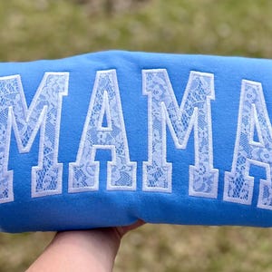 May include: A light blue sweatshirt with the word "MAMA" embroidered in white lace.
