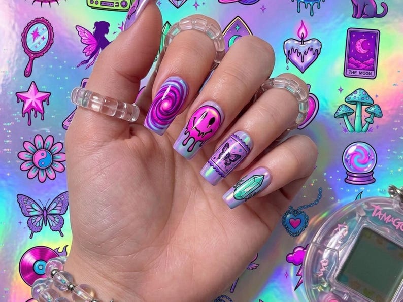 Puede incluir: Una mano con u&ntilde;as largas de forma cuadrada con dise&ntilde;os vibrantes en morado, rosa y azul que incluyen una espiral, una cara sonriente que se derrite, una mariposa y un cristal. La mano lleva tres anillos de pl&aacute;stico transparente y una pulsera.