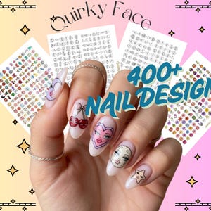 Puede incluir: Un conjunto de hojas de pegatinas para uñas con varias ilustraciones gráficas pequeñas, incluyendo cerezas, corazones, lunas y estrellas. El texto Quirky Face y 400+ NAIL DESIGNS está impreso en la imagen. Las pegatinas se muestran en las uñas.