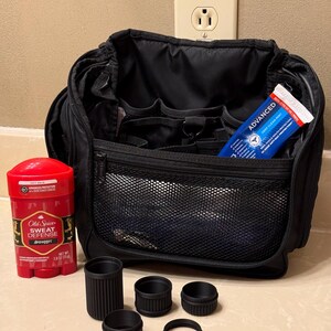 May include: Black travel bag with multiple compartments, a red and black Old Spice deodorant stick, and a tube of Advanced Deep Clean Mint toothpaste. There are also five black cylindrical objects of varying sizes.