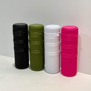 May include: Four cylindrical containers in black, olive green, white, and hot pink. Each container has a ribbed texture and a matching lid. The containers are standing upright against a white background.