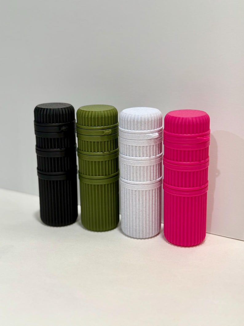 May include: Four cylindrical containers in black, olive green, white, and hot pink. Each container has a ribbed texture and a matching lid. The containers are standing upright against a white background.