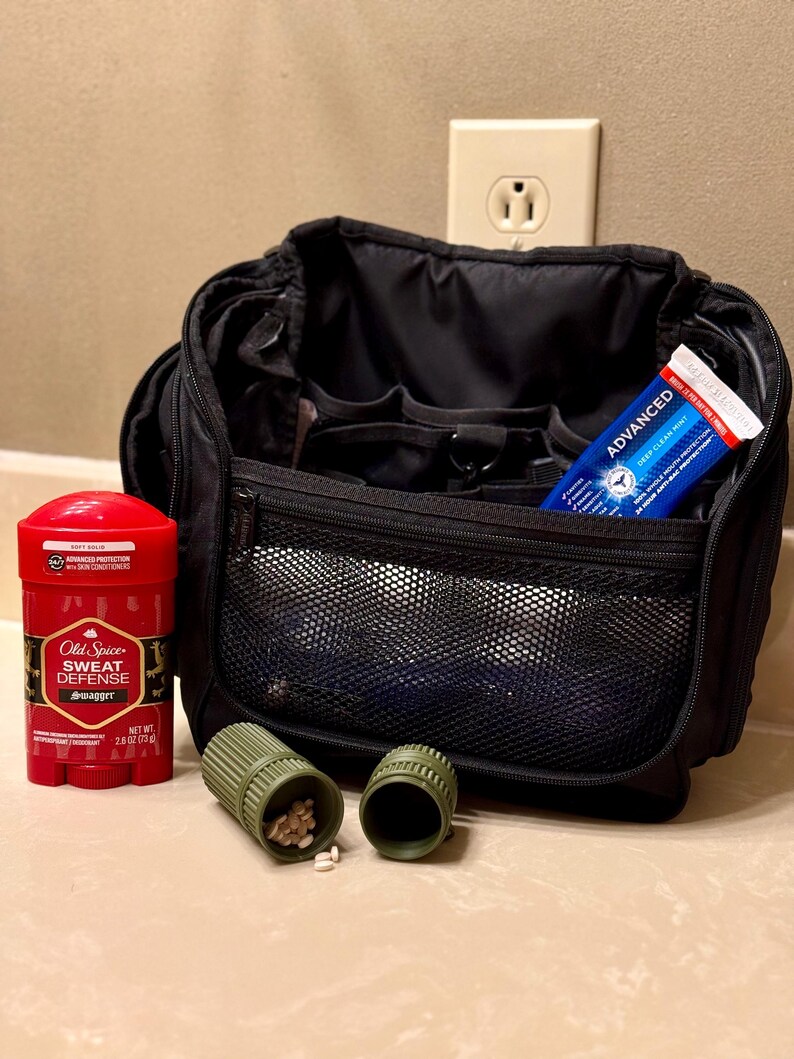 May include: A black travel bag with various compartments, a red deodorant stick, a tube of toothpaste, and two green pill containers. The deodorant is labelled "Old Spice Sweat Defense Swagger". The toothpaste is labelled "Advanced Deep Clean Mint".