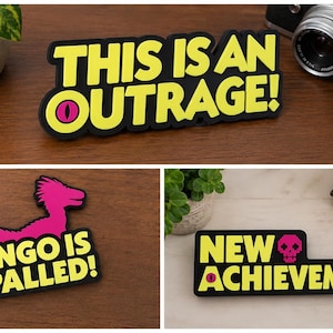 May include: Three black rectangular stickers with yellow text and black borders. The stickers say "THIS IS AN OUTRAGE!", "MONGO IS APPALLED!", and "NEW ACHIEVEMENT!". Each sticker has a unique graphic, including a dinosaur.