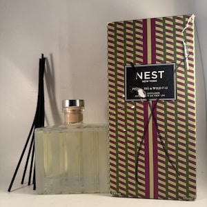 May include: A rectangular glass diffuser bottle with a silver cap and wooden stopper, accompanied by black reeds and a patterned box. The box features a green and burgundy geometric design with the text "NEST NEW YORK PISTACHIO & WILD FIG DIFFUSER". The bottle contains 5.9 fl oz.